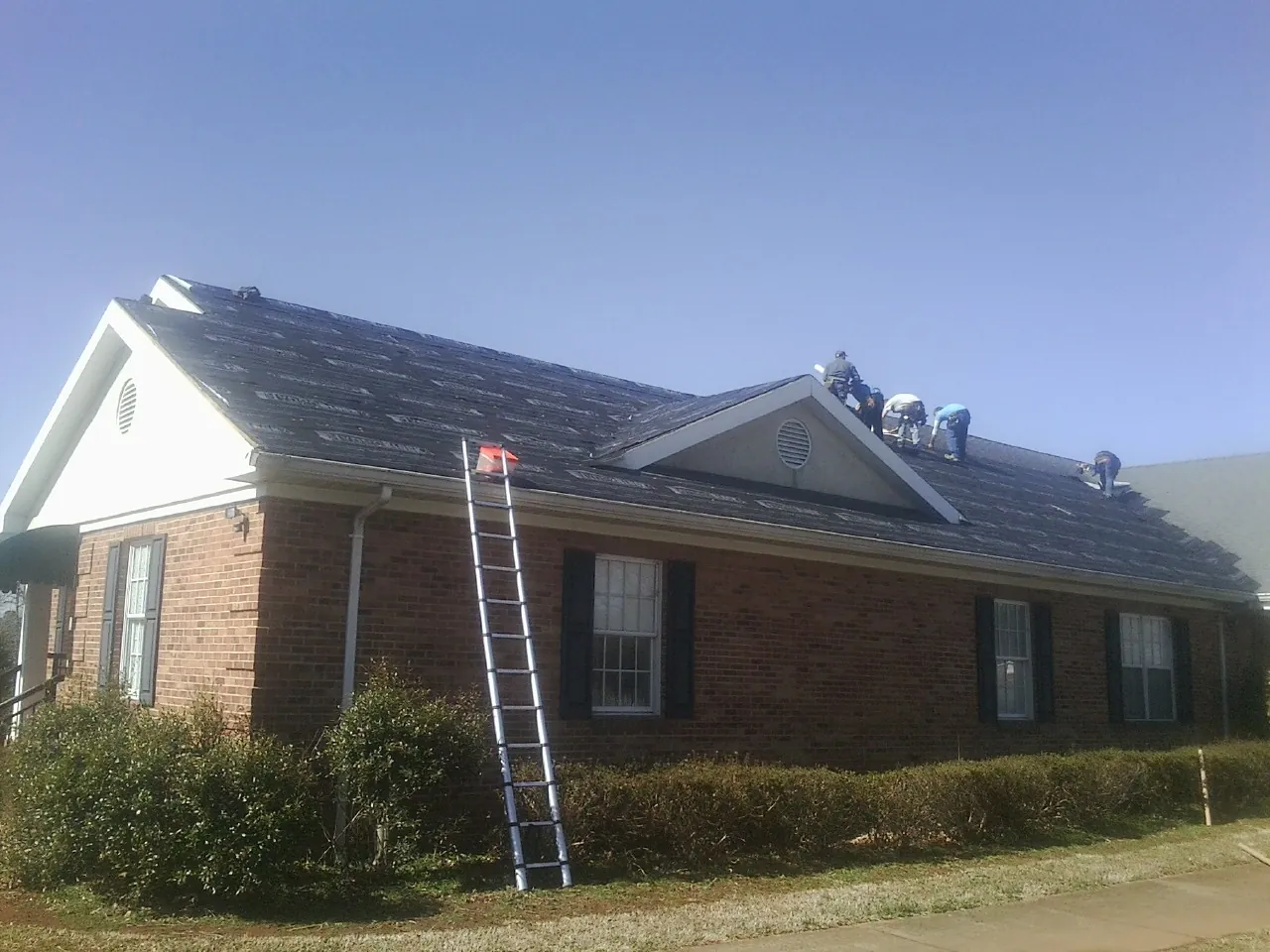 Crew tearing shingles off a brick ranch roof with a ladder set — Metal Roof Repair work by our crew in Tomkins Cove