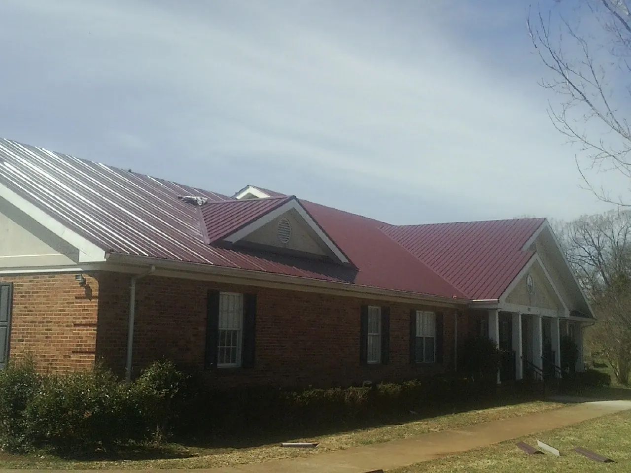 Red metal roof with gabled entries on a long brick building, from a Hail Damage Roof Repair job in Tomkins Cove