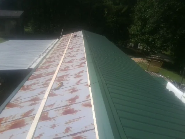 Old rusted panels beside newly installed green metal roofing — Wind Damage Roof Repair by Roofing Brothers in Tomkins Cove