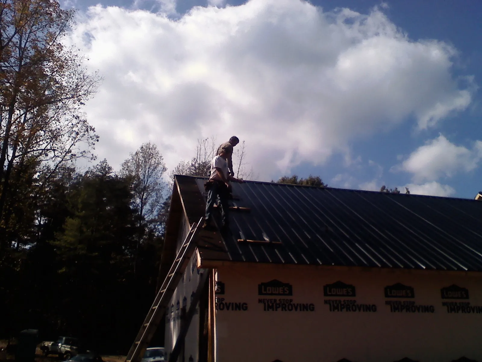 Roofer fastening dark metal panels high against a cloudy sky, from a Roof Inspection job in Tomkins Cove
