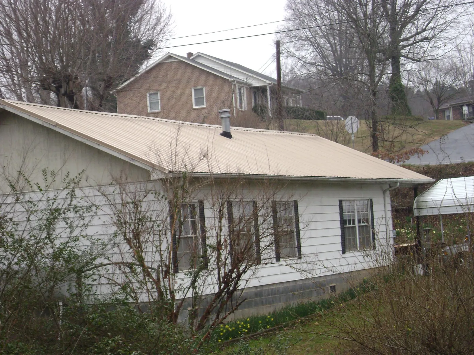 Tan metal roof on a white sided house set into a hillside — Commercial Roofing by Roofing Brothers in Tomkins Cove